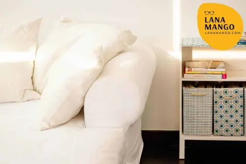 Sofá blanco con cojines y estantería con libros y cestas. Ideas para como hacer funda sofa.