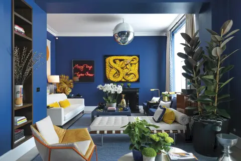 El azul vibrante de las paredes crea un telón de fondo audaz. El amarillo mostaza y el blanco puro son colores que combinan con el azul, aportando calidez y luminosidad a este salón moderno.