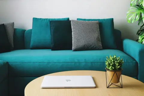 Un sofá moderno color turquesa, con cojines en tonos oscuros y un patrón de pata de gallo. Un portátil y una planta decoran la mesa de centro. ¡Perfecto para teñir el sofá de un nuevo color!