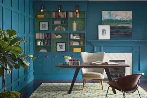 Estudio con paredes y estanterías en azul petróleo, combinación perfecta con detalles verdes. Alfombra geométrica y mobiliario moderno.