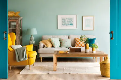 Un salón moderno donde se combinan mostaza y azul en cojines, sillón y puerta.
