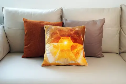 Tres cojines sobre un sofá de cuero: uno naranja texturizado, uno con un diseño de cristal amarillo brillante y otro marrón. El cojín central, con su estampado de velour que es, irradia calidez.