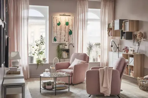 Acogedor salón rosa palo y gris con sillones cómodos, mesa de centro de cristal y estanterías llenas de libros y plantas.