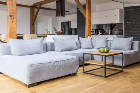 Sofá gris moderno con cojines, mesa de centro de madera y metal. Ideas para como hacer fundas de sofas faciles.