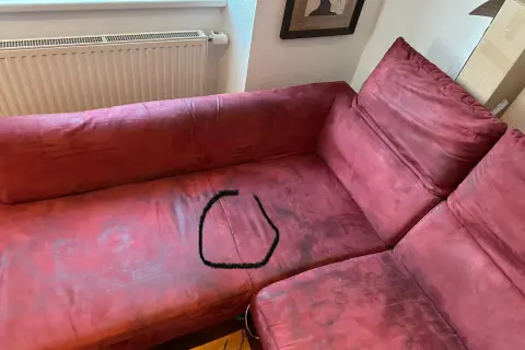 Un sofá de tela rojo con una mancha negra en forma de círculo. ¿Cómo reparar un sofá de tela roto?