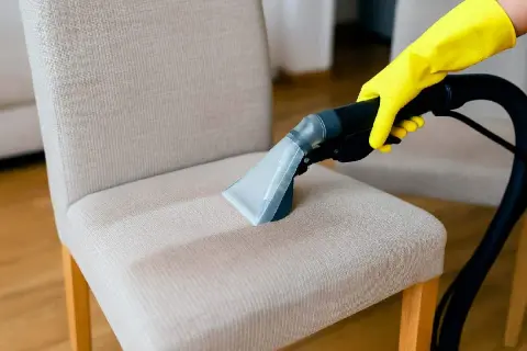 Mano con guante amarillo usando aspiradora para limpiar tapicería de sillón.