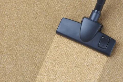 Cabezal de aspiradora limpiando una alfombra beige. Aprende como limpiar la alfombra en casa para un hogar impecable.