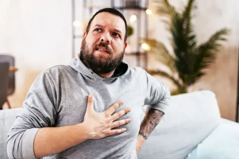Hombre con barba, con la mano en el pecho, con expresión de dolor. Estaba durmiendo y de repente me desperté sin poder respirar.