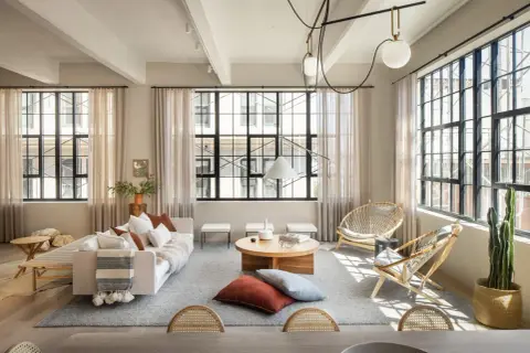 Un salón estilo industrial nórdico con sofá blanco, mesas de centro de madera, sillas de ratán y grandes ventanales.