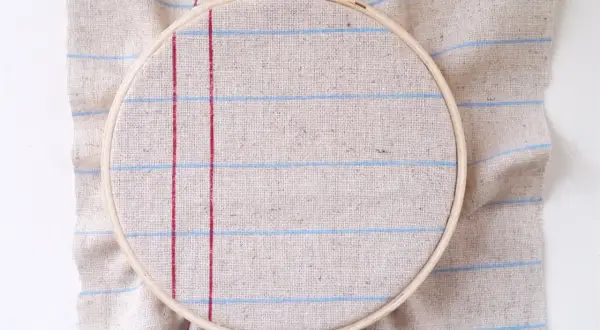 Bastidor de bordar sobre tela de lino con líneas rojas y azules, ideal para tus proyectos de hogar manualidades para casa.