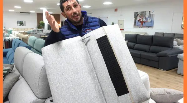 Hombre muestra cómo desmontar chaise longue. En el fondo, sofás de exposición.