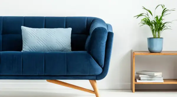 Sofá azul profundo con cojín claro. Un toque de color turquesa en la decoración con una planta y libros en una mesita de madera.