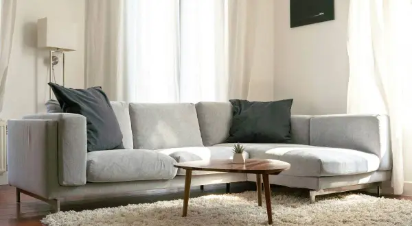 Sofá gris con cojines oscuros, alfombra mullida y mesa de centro. Un lugar acogedor, pero cuidado con los ácaros del sofá.