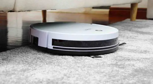 Robot aspirador blanco y negro limpiando alfombra gris, ideal para saber como eliminar los acaros del hogar.