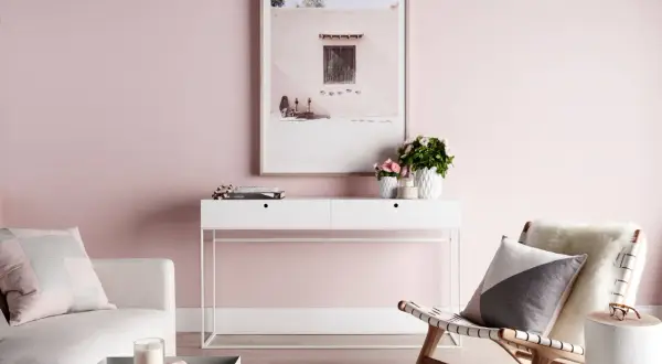 Un salón con paredes rosas, un sofá blanco, una consola con flores y un cuadro. El rosa se combina con blanco, gris y madera para un ambiente sereno.
