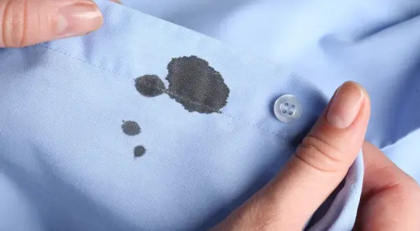 Manos sujetan camisa azul con manchas de boli. Aprende como quitar manchas de boli fácilmente.