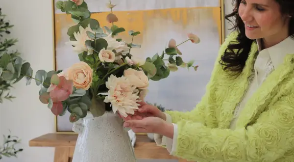 Mujer sonriente arregla un ramo de flores de tela, mostrando cómo limpiar flores de tela para mantener su belleza.
