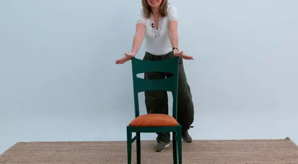 Mujer sonriente muestra cómo forrar sillas con estilo, usando una silla verde con cojín naranja.