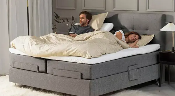 Hombre despierto en cama con portátil, mujer durmiendo a su lado. Un momento de paz para dormir juntos.