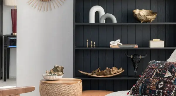 Estantería oscura con objetos decorativos en tonos tierra y dorados, mezclando muebles de distintos colores y texturas para un estilo ecléctico.