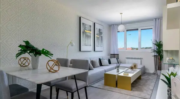 Salón rectangular dos ambientes con mesa de mármol, sofá modular gris y mesas doradas.