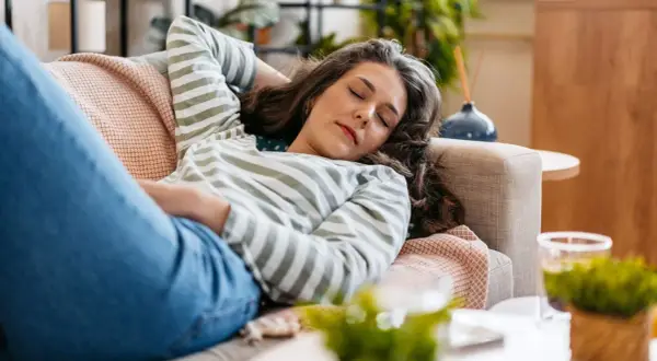 Mujer descansando en el sofá, con los ojos cerrados, lista para dormir antes de comer.