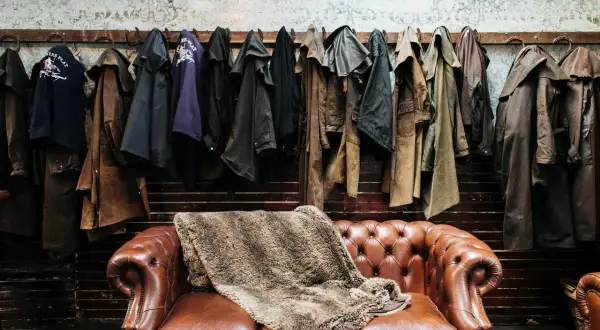 Abrigos de cuero colgados sobre un sofá Chesterfield. Si el cuero huele, aquí te explicamos como quitar el olor a cuero.