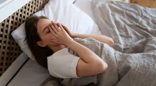 Mujer en la cama, con las manos cubriendo su rostro, luchando contra el miedo a quedarse dormido.