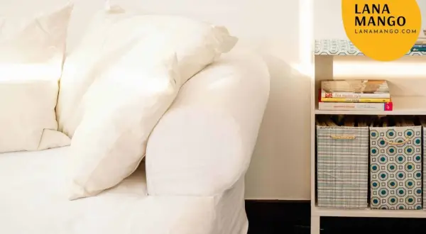 Sofá blanco con cojines y estantería con libros y cestas. Ideas para como hacer funda sofa.