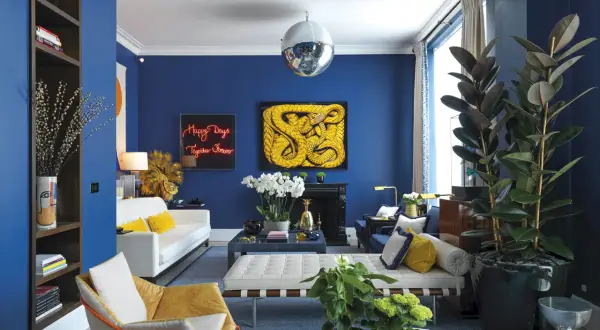 El azul vibrante de las paredes crea un telón de fondo audaz. El amarillo mostaza y el blanco puro son colores que combinan con el azul, aportando calidez y luminosidad a este salón moderno.