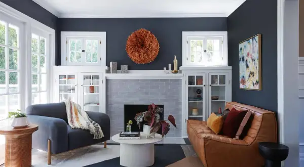 Ideas para decorar rincones pequeños: un sofá de cuero, sillón gris, chimenea y arte abstracto en un salón moderno.
