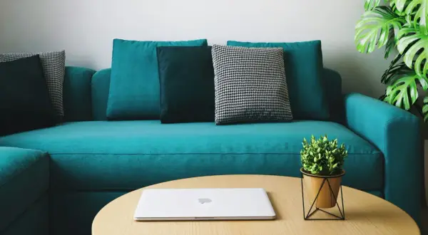 Un sofá moderno color turquesa, con cojines en tonos oscuros y un patrón de pata de gallo. Un portátil y una planta decoran la mesa de centro. ¡Perfecto para teñir el sofá de un nuevo color!