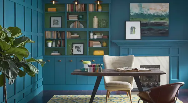Estudio con paredes y estanterías en azul petróleo, combinación perfecta con detalles verdes. Alfombra geométrica y mobiliario moderno.
