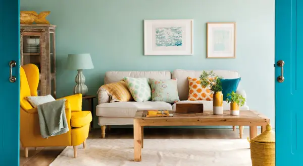 Un salón moderno donde se combinan mostaza y azul en cojines, sillón y puerta.
