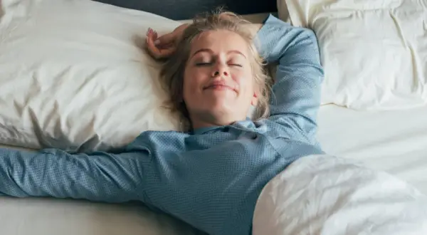 Mujer rubia sonríe plácidamente en su cama, disfrutando de un sueño reparador bajo la suave roba de llit.
