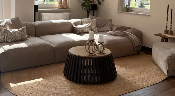 Alfombra redonda de yute planta bajo un sofá modular beige. La luz del sol ilumina la sala.