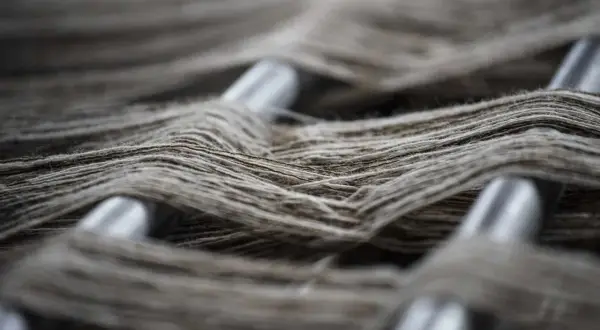 Fibras sintéticas ejemplos: hilos grises entrelazados sobre barras metálicas, creando una textura visual rica y detallada.