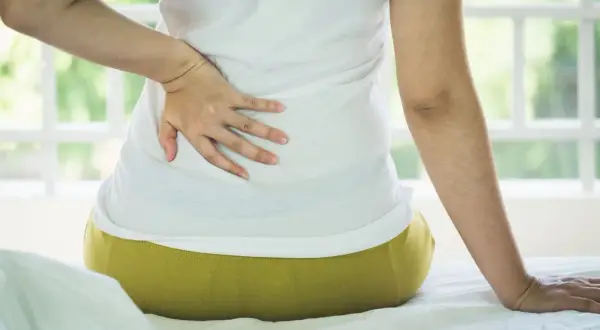 Persona con dolor de espalda, buscando cómo dormir con escoliosis.