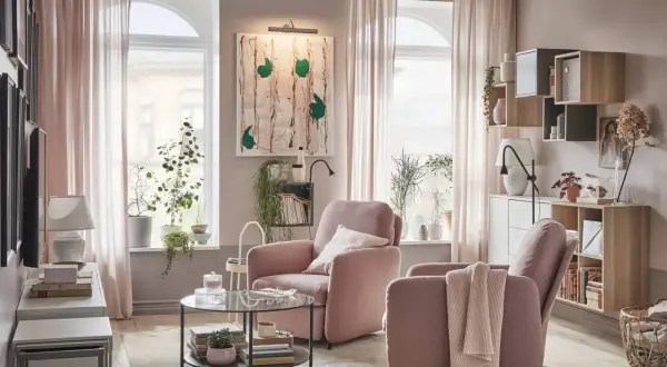 Acogedor salón rosa palo y gris con sillones cómodos, mesa de centro de cristal y estanterías llenas de libros y plantas.