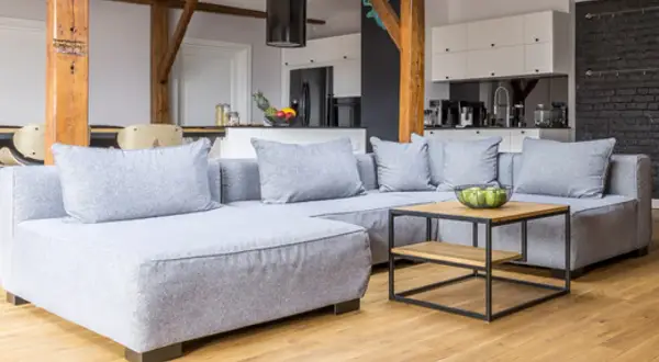 Sofá gris moderno con cojines, mesa de centro de madera y metal. Ideas para como hacer fundas de sofas faciles.