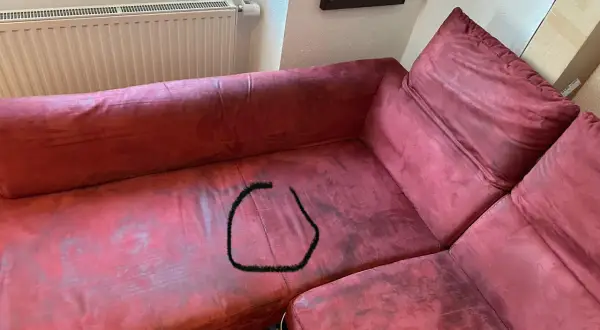 Un sofá de tela rojo con una mancha negra en forma de círculo. ¿Cómo reparar un sofá de tela roto?