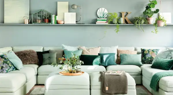 Sofá modular con cojines en tonos verdes y marrones, creando una paleta de colores que combinan con turquesa. Plantas y objetos decorativos en una estantería superior.