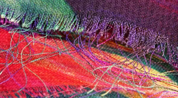Detalle de tela con hilos sueltos de colores vibrantes. Se aprecia el tejido y cómo se puede coser a mano para que no se deshilache.