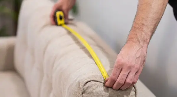 Persona mide un sofá con cinta métrica para saber como medir sofá para fundas.