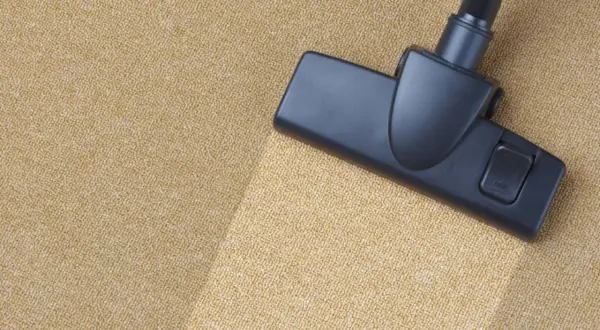 Cabezal de aspiradora limpiando una alfombra beige. Aprende como limpiar la alfombra en casa para un hogar impecable.