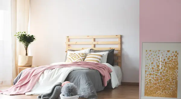 Dormitorio acogedor donde el beige y rosa combinan a la perfección en mantas y cojines. Una planta aporta frescura.