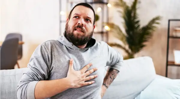 Hombre con barba, con la mano en el pecho, con expresión de dolor. Estaba durmiendo y de repente me desperté sin poder respirar.