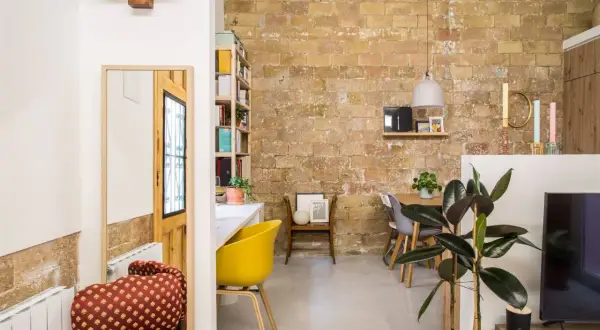 Acogedor loft de 40 metros cuadrados con pared de ladrillo visto, comedor, zona de trabajo y plantas.