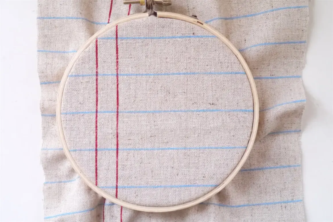 Bastidor de bordar sobre tela de lino con líneas rojas y azules, ideal para tus proyectos de hogar manualidades para casa.