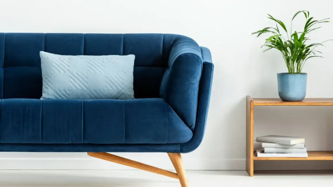 Sofá azul profundo con cojín claro. Un toque de color turquesa en la decoración con una planta y libros en una mesita de madera.